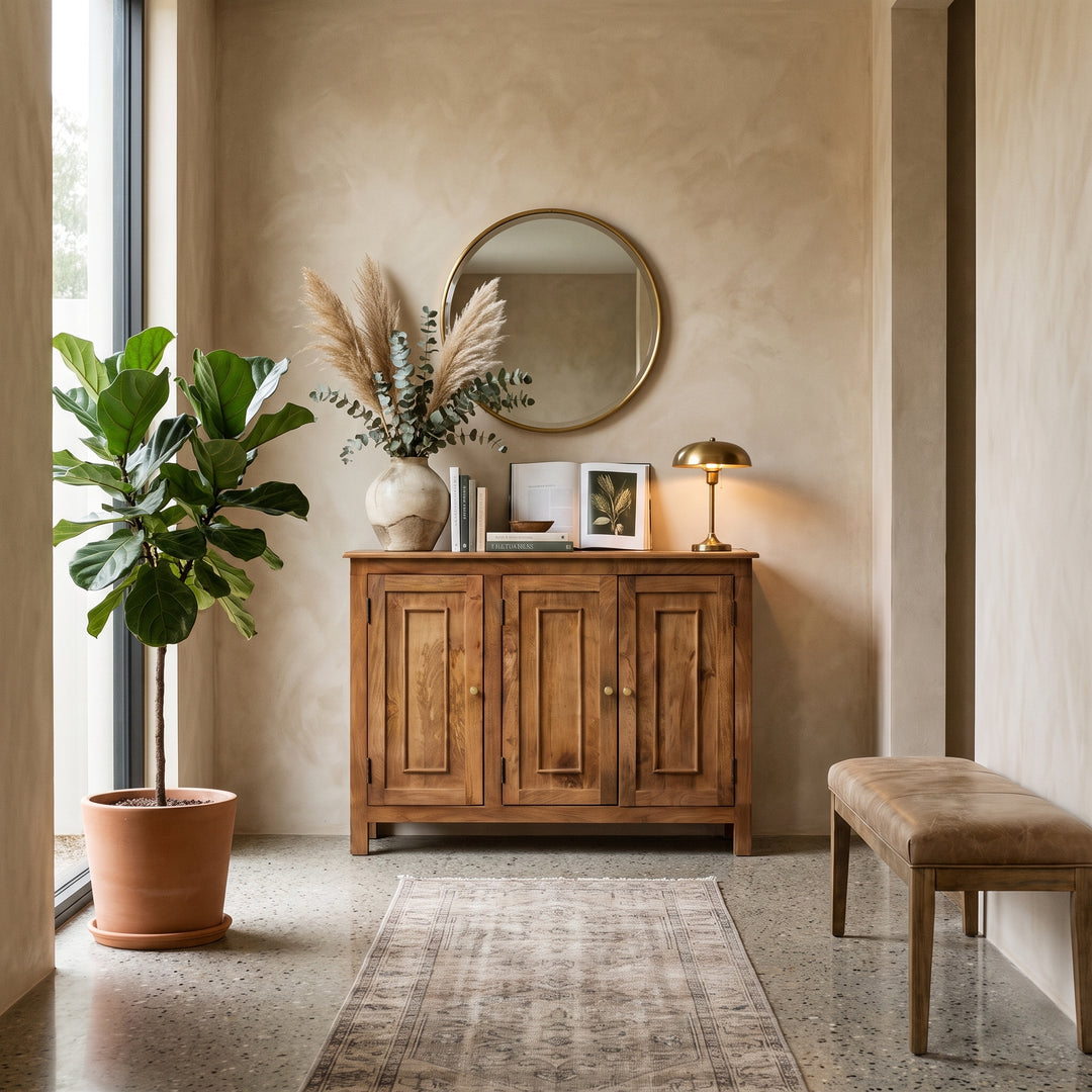 Modern entryway with a wooden console table, round mirror, fiddle leaf fig plant, and leather bench in a warm, minimalist home.