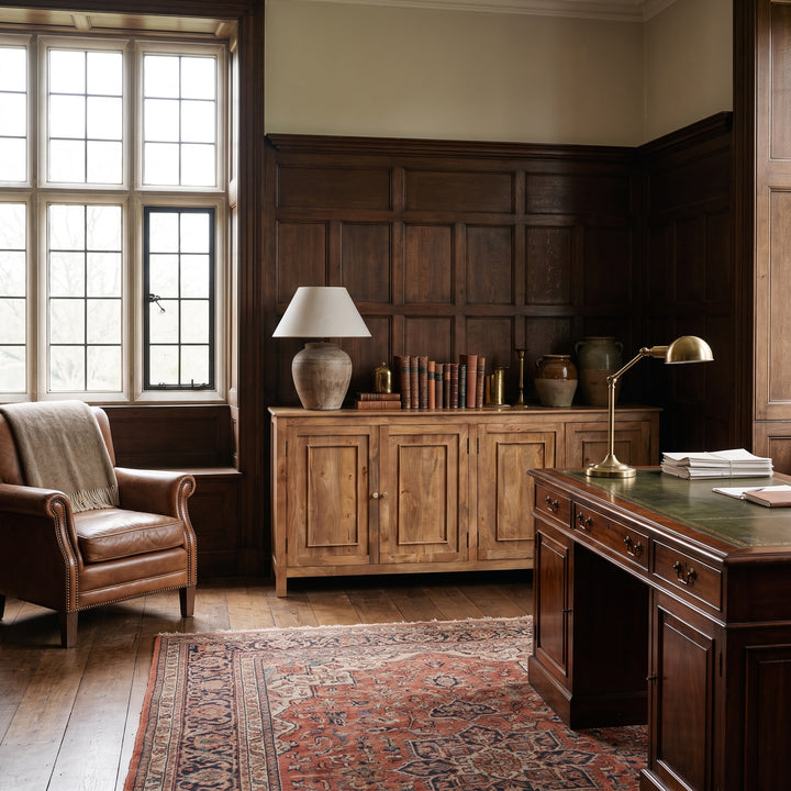 Classic home office with wood paneling, leather armchair, antique desk, and patterned rug in a traditional study.