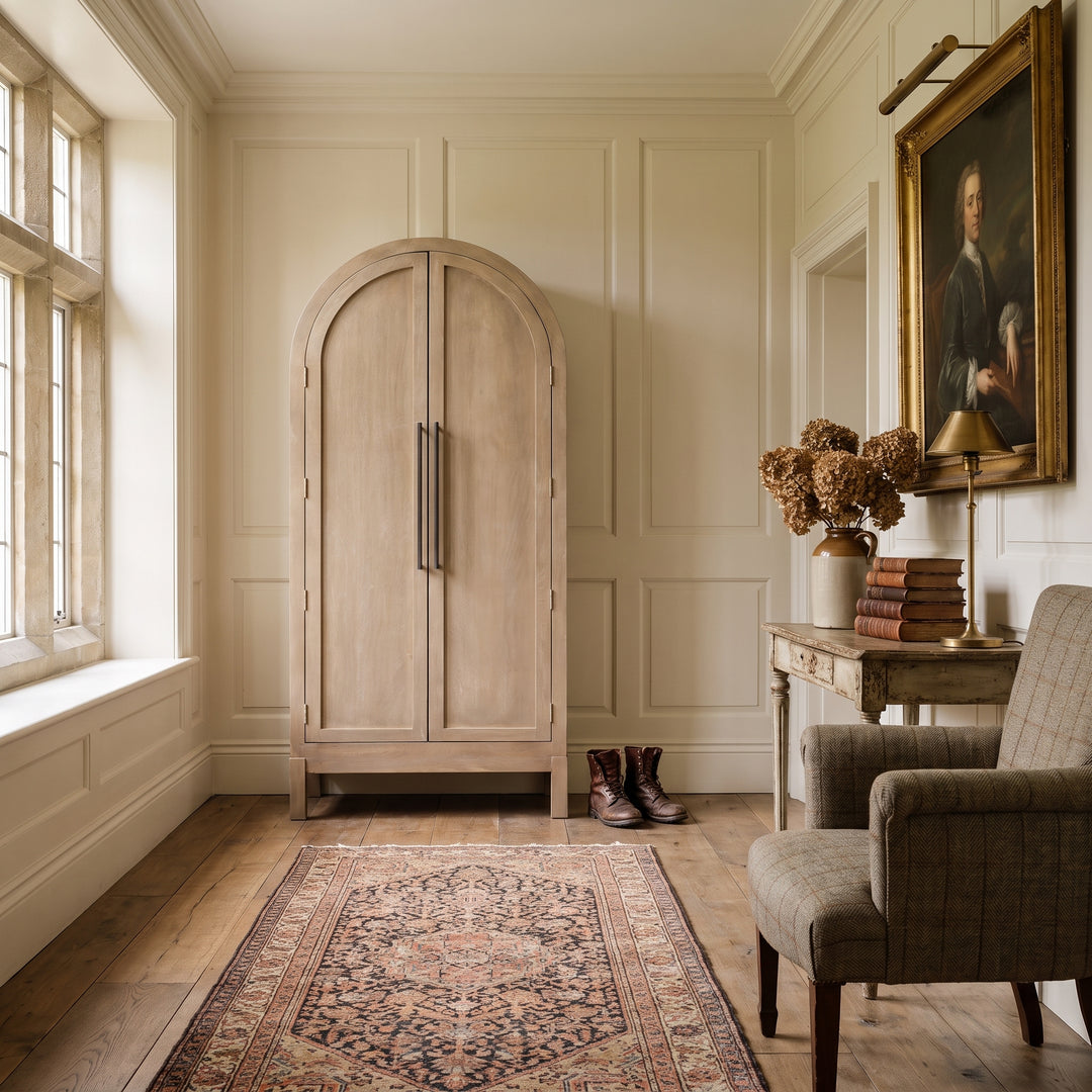 Elegant entryway with an arched wooden wardrobe, vintage armchair, antique portrait, and Persian rug in a classic home.