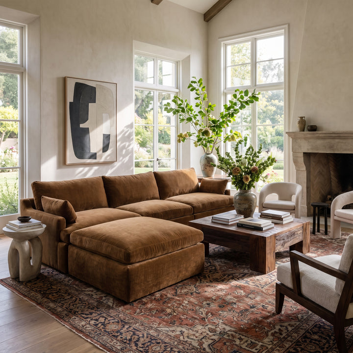 Modern rustic living room featuring a plush brown velvet sectional, vintage rug, stone fireplace, and natural light.