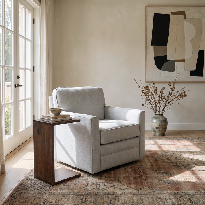 Modern living room corner featuring a light gray swivel chair, a wooden C-table, and abstract wall art on a vintage rug.