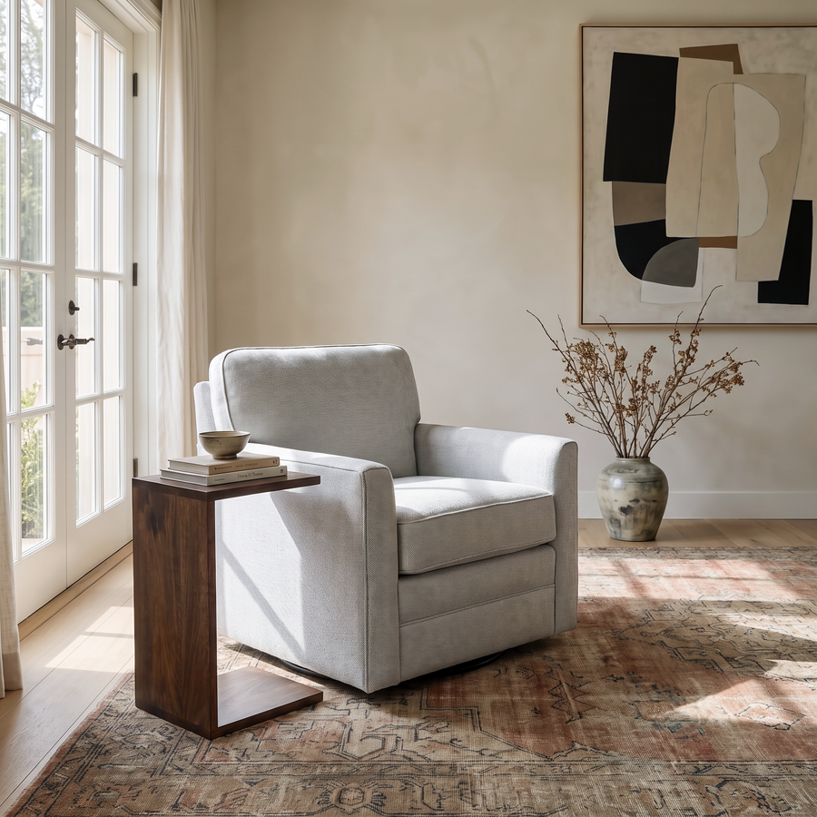 Modern living room corner featuring a light gray swivel chair, a wooden C-table, and abstract wall art on a vintage rug.