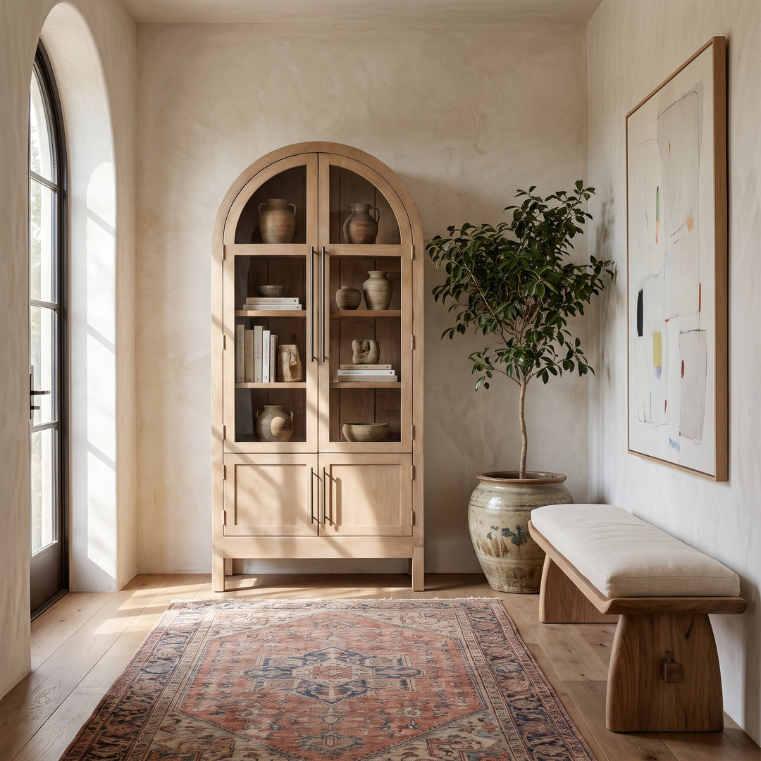 Modern entryway with an arched wooden cabinet, a beige upholstered bench, an abstract painting, and a vintage-style area rug.