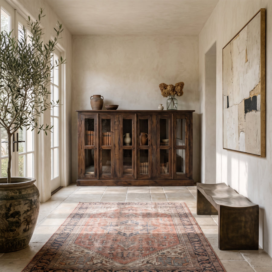 Elegant Mediterranean-style entryway featuring a wooden cabinet, vintage rug, olive tree, and abstract wall art.
