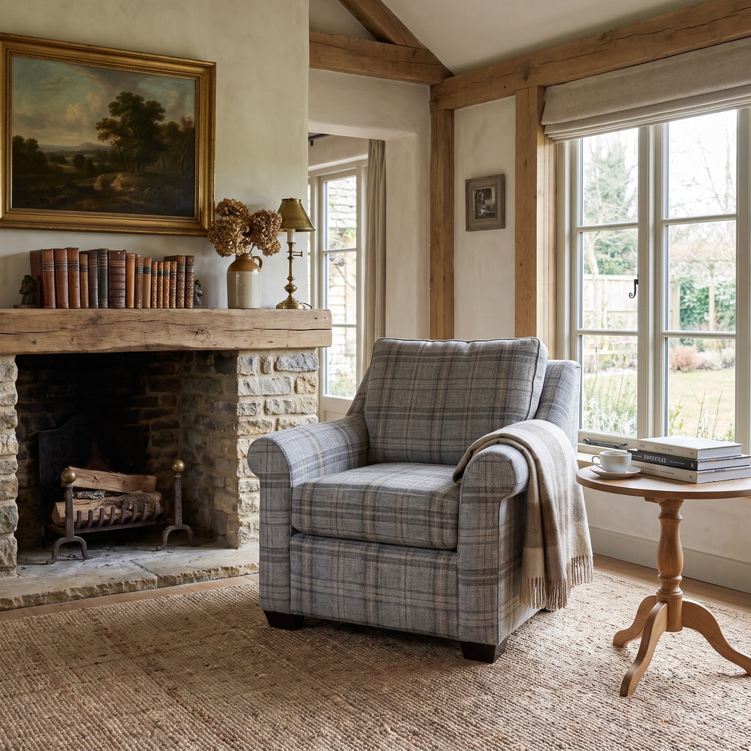 Cozy rustic living room featuring a plaid armchair, stone fireplace, wooden beams, and a bright window with garden views.