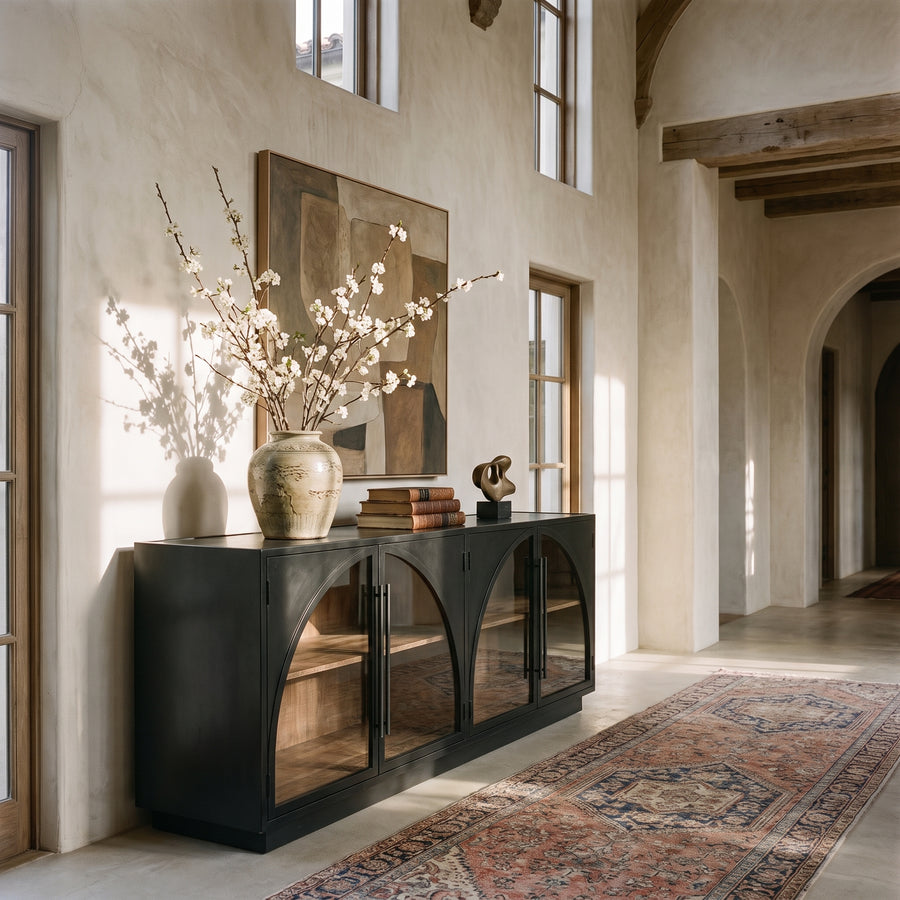 Modern Mediterranean entryway featuring a black arched console table, abstract art, and a vintage-style runner rug.