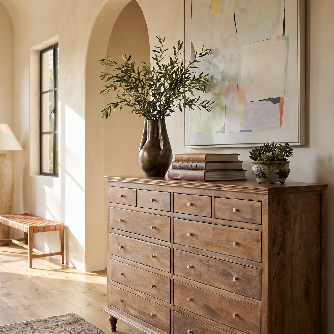 Modern Mediterranean entryway featuring a wooden dresser, olive branch vase, abstract art, and a woven bench in a bright room.